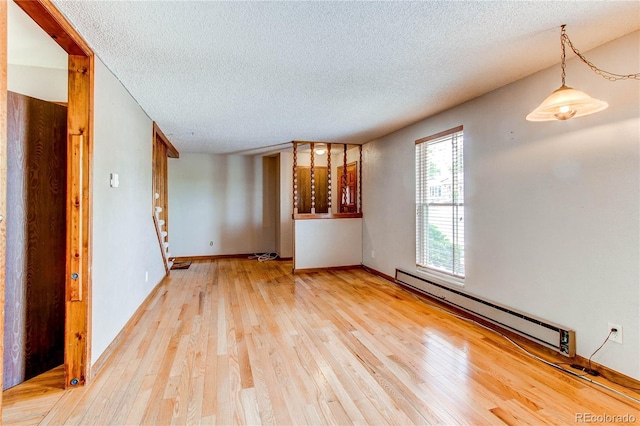 empty room featuring a baseboard heating unit, a textured ceiling, light wood-style flooring, and baseboards