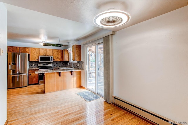 kitchen featuring appliances with stainless steel finishes, baseboard heating, brown cabinets, backsplash, and a peninsula