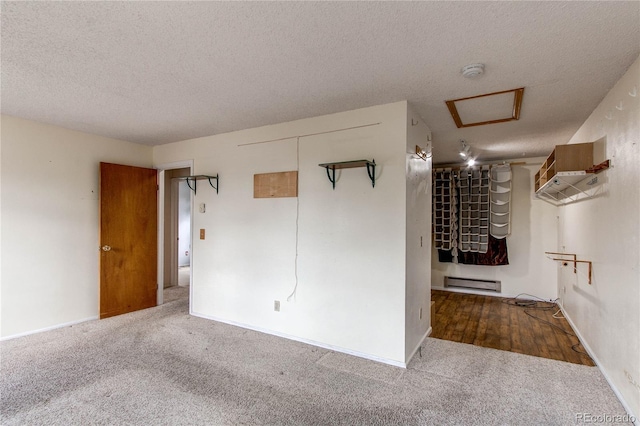 empty room featuring attic access, a textured ceiling, a baseboard heating unit, carpet, and a smoke detector