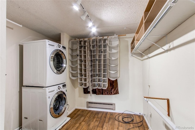 clothes washing area with baseboard heating, stacked washing machine and dryer, wood finished floors, a textured ceiling, and baseboards