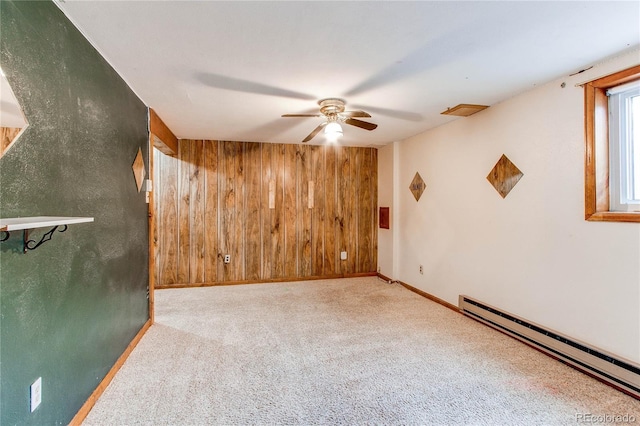 empty room featuring baseboard heating, wood walls, a ceiling fan, carpet, and baseboards