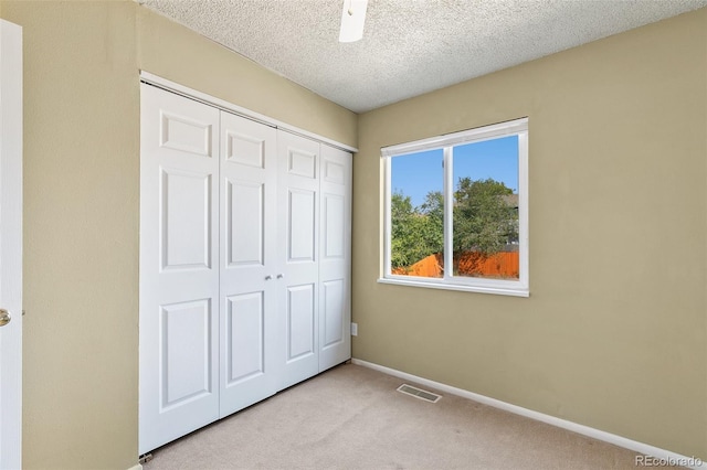 unfurnished bedroom with a closet, a textured ceiling, light colored carpet, and ceiling fan