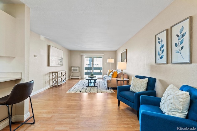 living room with a baseboard heating unit, a wall mounted air conditioner, a textured ceiling, and light wood-type flooring