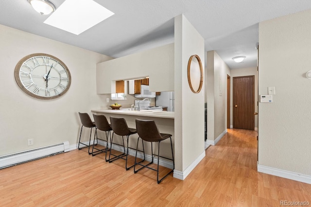 kitchen featuring a skylight, a breakfast bar, kitchen peninsula, and light wood-type flooring