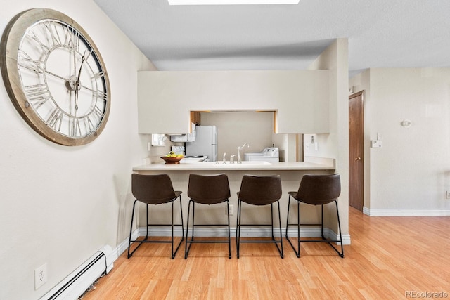 kitchen with a kitchen breakfast bar, light wood-type flooring, baseboard heating, and kitchen peninsula