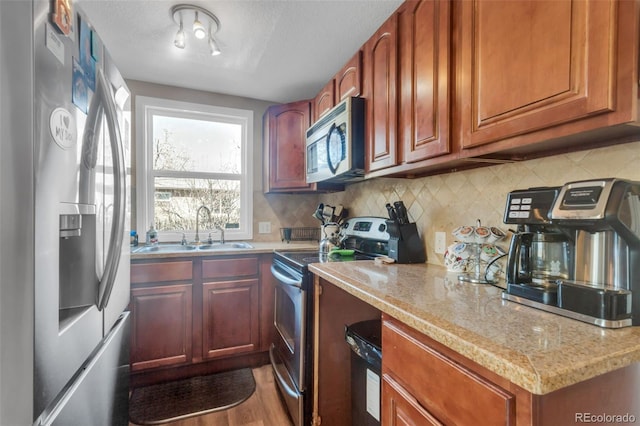 kitchen with tasteful backsplash, light stone counters, appliances with stainless steel finishes, wood finished floors, and a sink