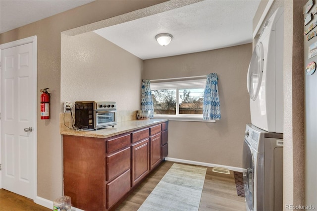 laundry area with visible vents, baseboards, a toaster, light wood-type flooring, and stacked washer and clothes dryer