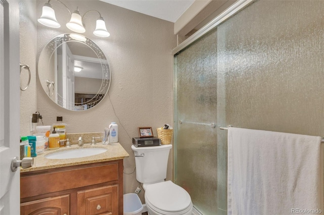 bathroom featuring toilet, a shower stall, vanity, and a textured wall