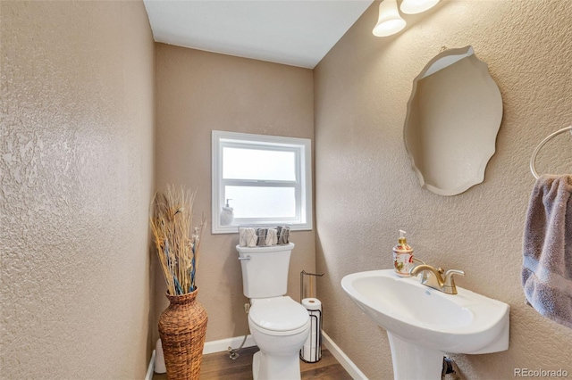 half bath featuring baseboards, toilet, wood finished floors, a textured wall, and a sink