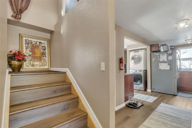 staircase featuring wood finished floors, baseboards, stacked washing maching and dryer, a textured ceiling, and a textured wall