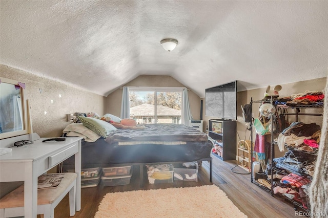 bedroom with a textured ceiling, wood finished floors, and vaulted ceiling