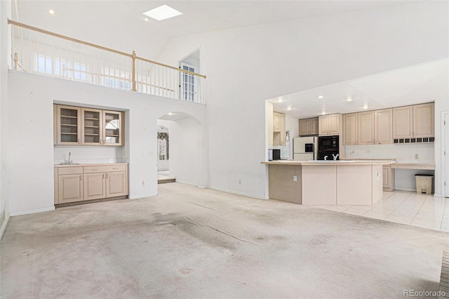 unfurnished living room featuring arched walkways, high vaulted ceiling, light carpet, and baseboards