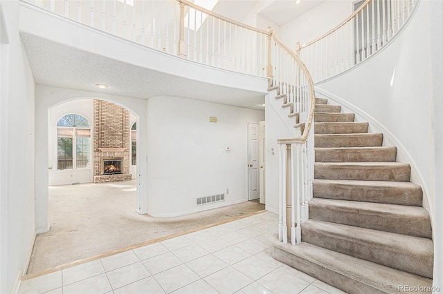 stairway with visible vents, a brick fireplace, a towering ceiling, baseboards, and carpet
