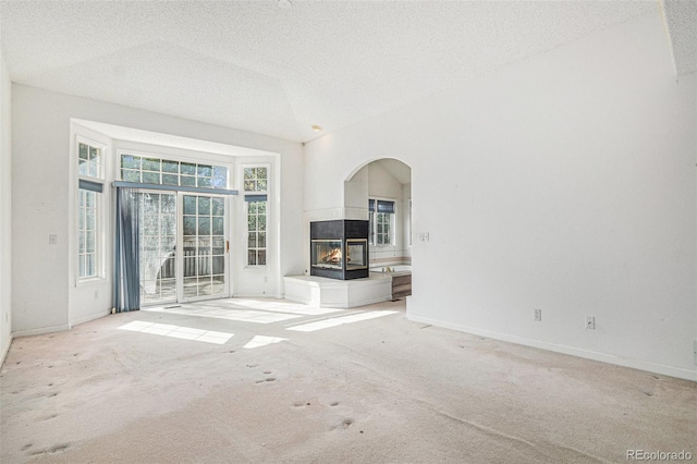 unfurnished living room featuring a multi sided fireplace, arched walkways, a textured ceiling, and light carpet