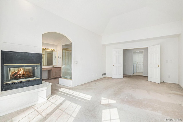 unfurnished living room featuring a multi sided fireplace, visible vents, arched walkways, baseboards, and light carpet