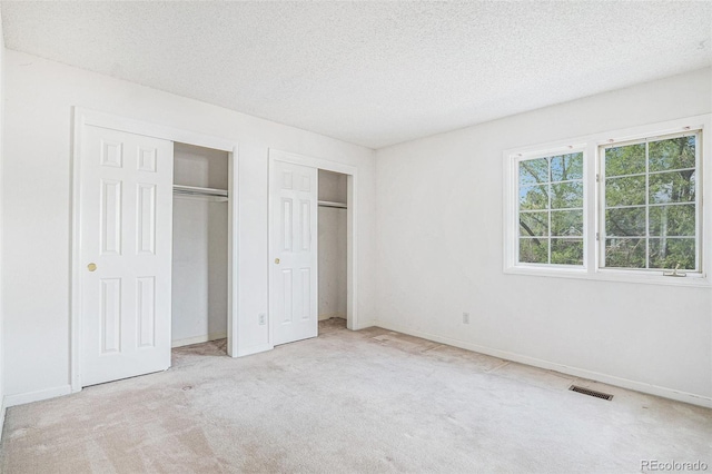 unfurnished bedroom with a textured ceiling, visible vents, carpet floors, baseboards, and two closets