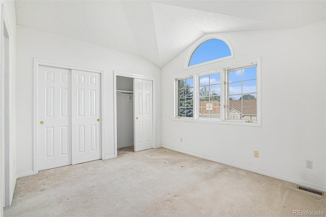 unfurnished bedroom featuring multiple closets, carpet, vaulted ceiling, and visible vents