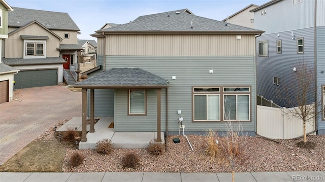 rear view of house with a garage, a shingled roof, fence, and decorative driveway