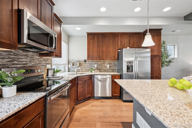 kitchen with light stone countertops, light wood finished floors, stainless steel appliances, and a sink