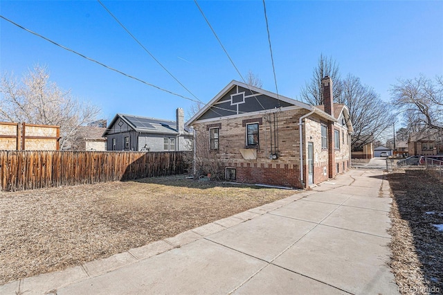 view of home's exterior with a chimney, fence, and brick siding