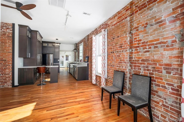 interior space with ceiling fan, rail lighting, brick wall, and light hardwood / wood-style flooring