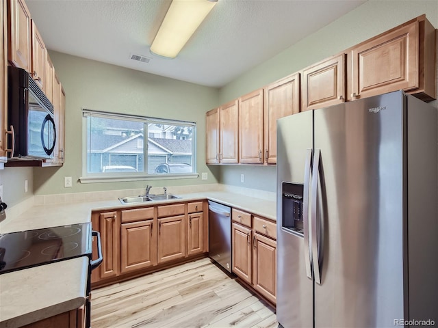 kitchen with a sink, stainless steel appliances, light wood-type flooring, visible vents, and light countertops