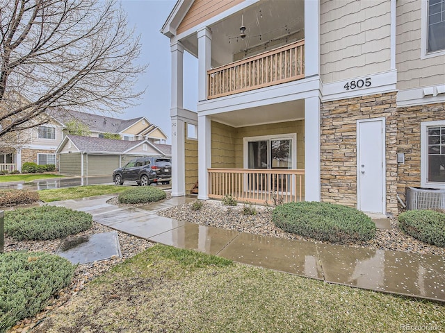 exterior space with central AC unit, stone siding, and a balcony
