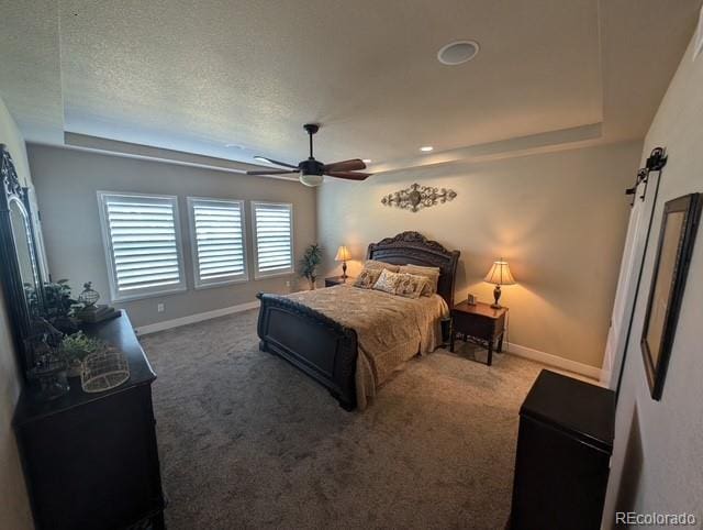 carpeted bedroom featuring a tray ceiling, ceiling fan, a textured ceiling, and baseboards