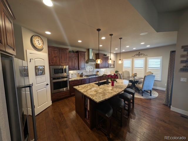 kitchen featuring wall chimney range hood, dark wood-style floors, appliances with stainless steel finishes, and a sink