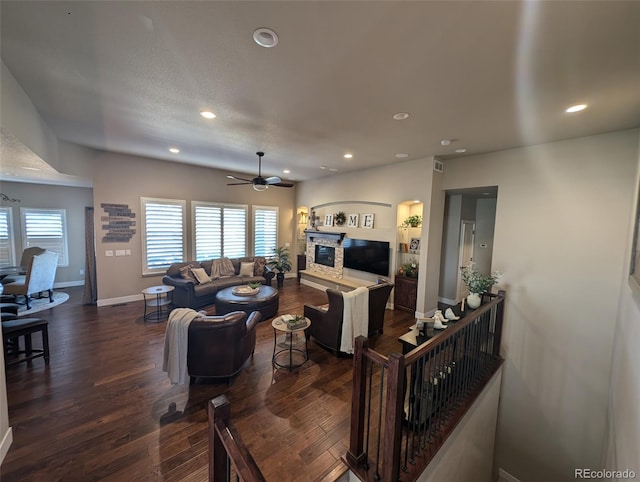 living room with a stone fireplace, dark wood-style flooring, and recessed lighting