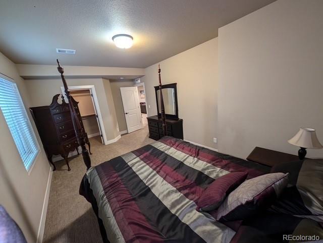 bedroom with baseboards, visible vents, a walk in closet, and light colored carpet