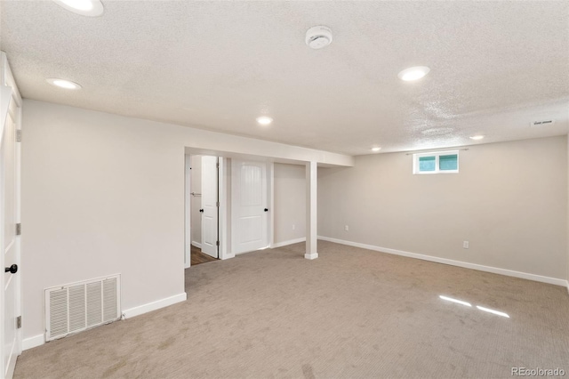 basement with a textured ceiling, recessed lighting, light colored carpet, visible vents, and baseboards