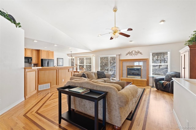 living room with ceiling fan with notable chandelier, a fireplace, lofted ceiling, and light wood-type flooring