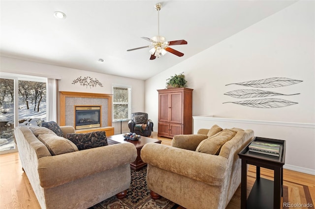 living room with ceiling fan, light wood-type flooring, a tile fireplace, and lofted ceiling