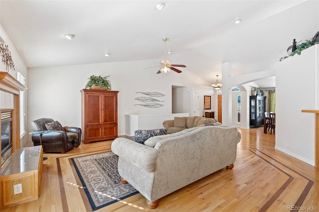 living room with lofted ceiling, a fireplace, light wood-type flooring, and ceiling fan