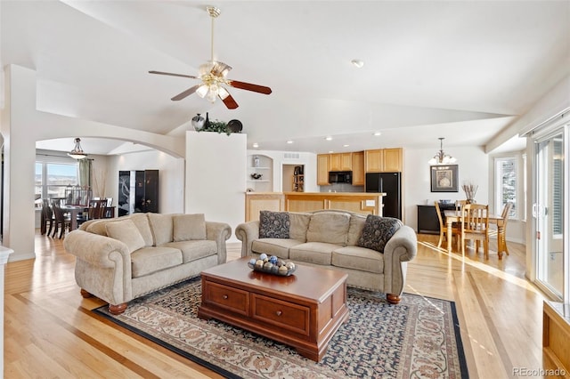 living room featuring ceiling fan with notable chandelier, vaulted ceiling, and light hardwood / wood-style flooring