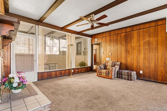 living area featuring wood walls, carpet flooring, beam ceiling, and ceiling fan