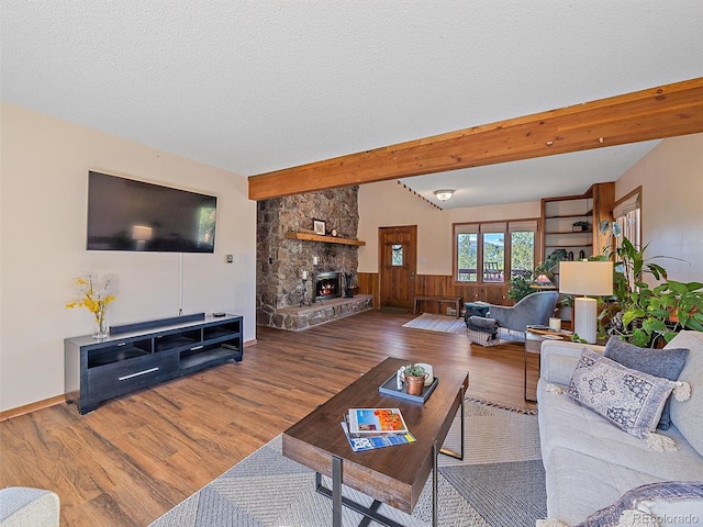 living room with a stone fireplace, a textured ceiling, beam ceiling, wooden walls, and hardwood / wood-style flooring