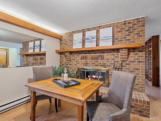 dining room with wood-type flooring, a fireplace, a textured ceiling, a baseboard heating unit, and brick wall