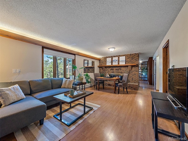 living room with a baseboard radiator, a textured ceiling, a fireplace, light hardwood / wood-style flooring, and brick wall