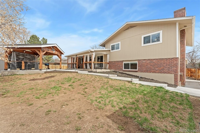 rear view of property featuring a gazebo, brick siding, a chimney, and fence