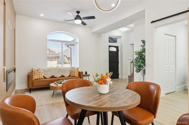 dining space with light hardwood / wood-style floors, a barn door, and ceiling fan