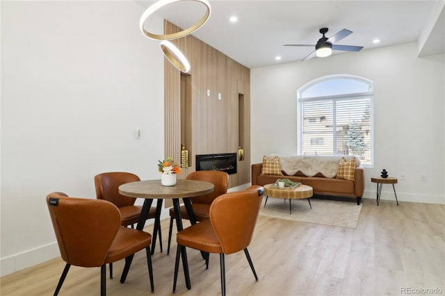 dining space featuring a large fireplace, ceiling fan, and light wood-type flooring