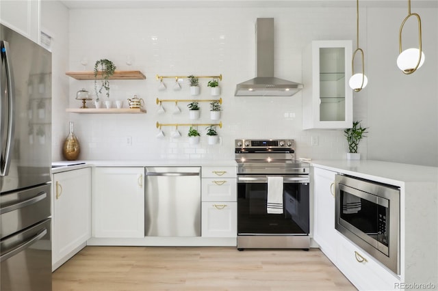 kitchen with wall chimney exhaust hood, white cabinetry, appliances with stainless steel finishes, pendant lighting, and backsplash