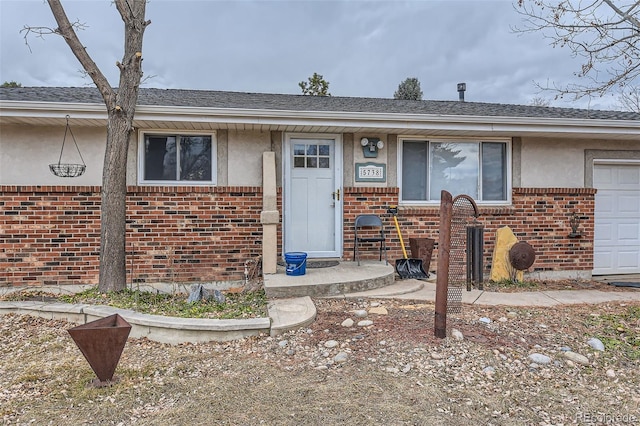 view of front of home featuring a garage, stucco siding, a shingled roof, and brick siding