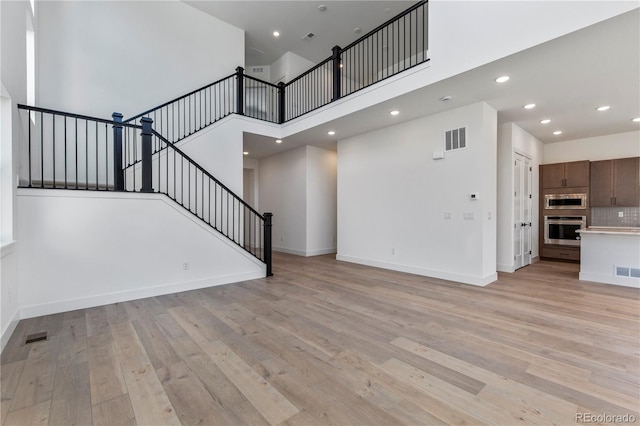 5626 W 142nd Ave, Broomfield, CO 80020 - unfurnished living room with stairs, a towering ceiling, light wood-style floors, and recessed lighting