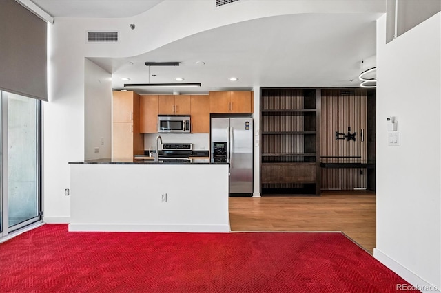 891 14th St Unit 2105, Denver, CO 80202 - kitchen featuring appliances with stainless steel finishes, dark countertops, brown cabinetry, a peninsula, and wood finished floors