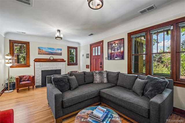 living area featuring light wood finished floors, a brick fireplace, and baseboards