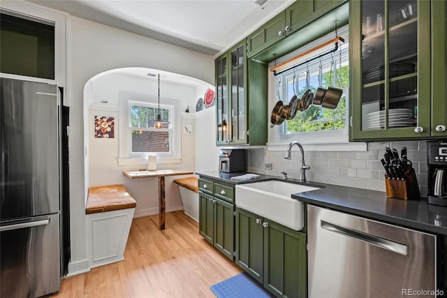kitchen with green cabinets, appliances with stainless steel finishes, a sink, decorative backsplash, and light wood-style flooring