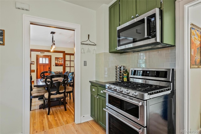 kitchen featuring green cabinets, stainless steel appliances, decorative backsplash, light wood-type flooring, and dark countertops
